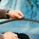 Imagem focada na mão de um homem com relógio de pulso trocando a palheta do para-brisa de um carro