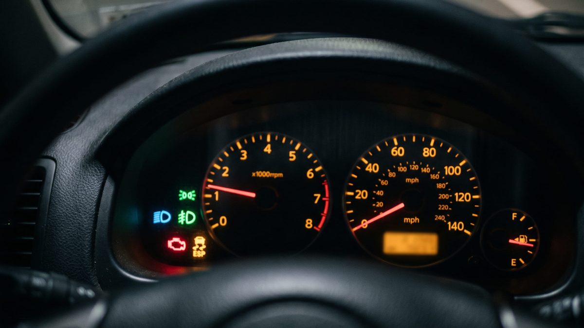 Painel de instrumentos de um carro com várias luzes de advertência acesas, visto através do volante, incluindo tacômetro e velocímetro iluminados.