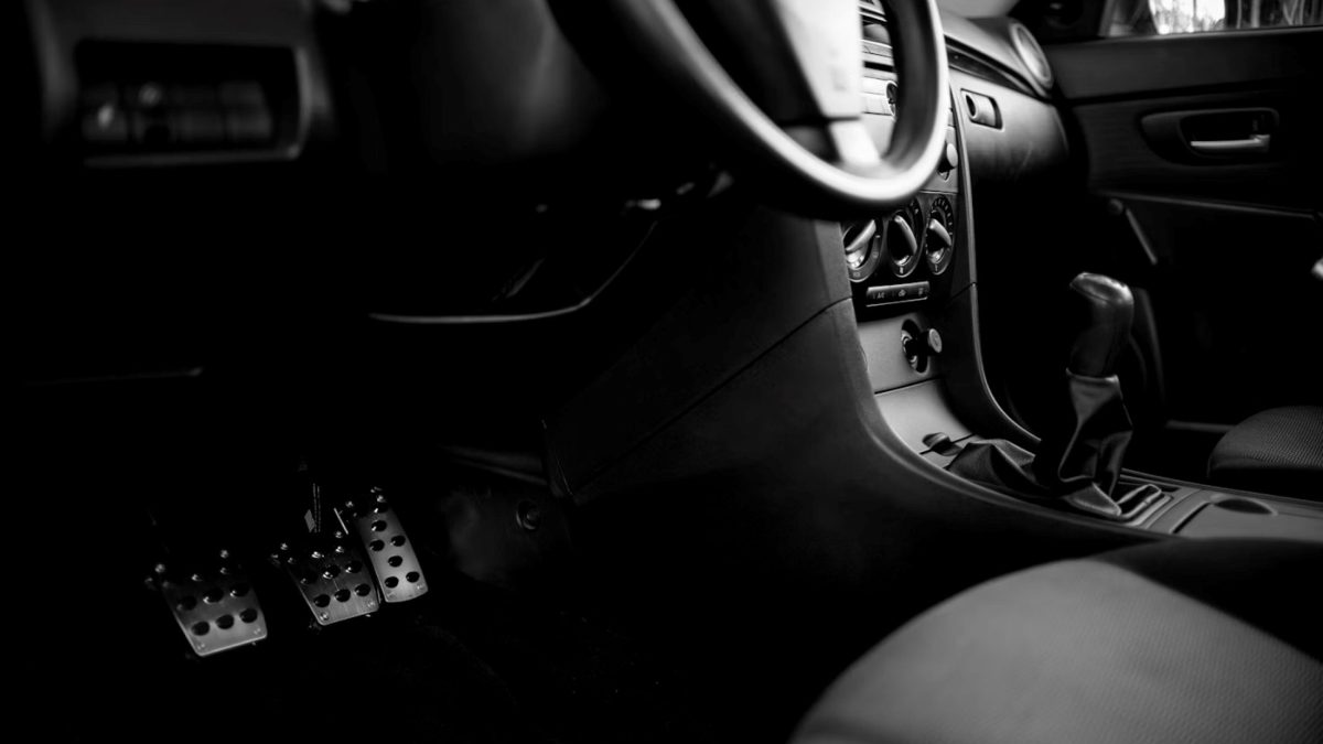 Interior de carro manual com volante, câmbio e pedais, incluindo o pedal da embreagem.