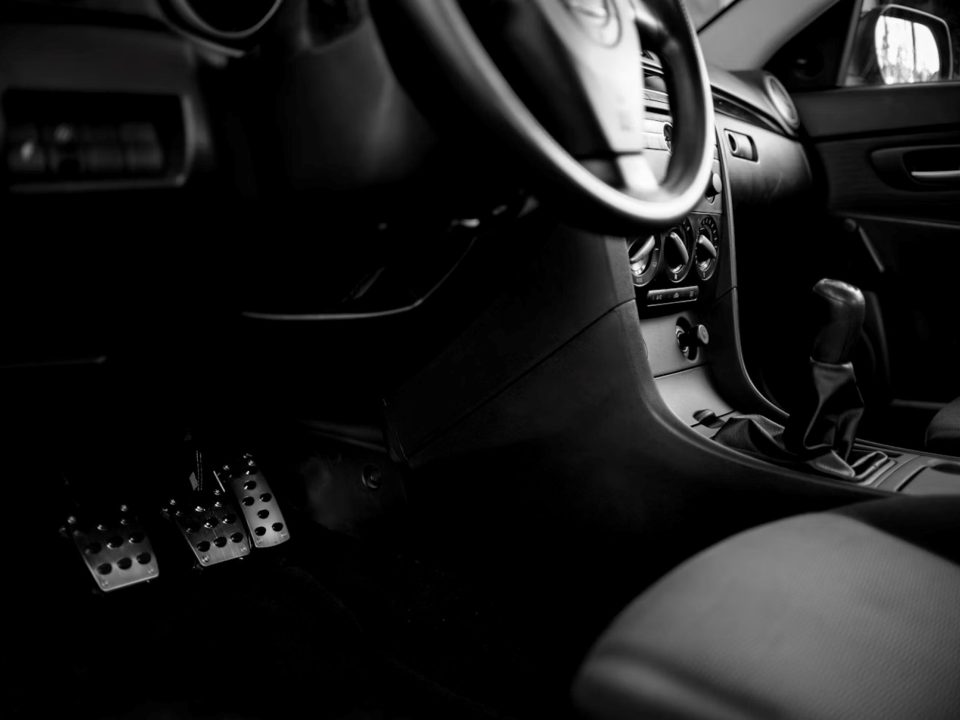 Interior de carro manual com volante, câmbio e pedais, incluindo o pedal da embreagem.