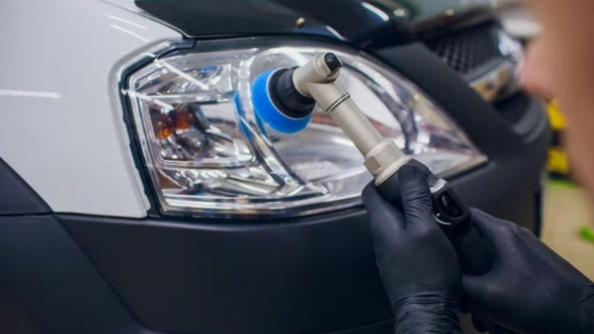 Profissional com luvas pretas usando politriz com boina azul para polir o farol de um carro branco.