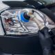 Profissional com luvas pretas usando politriz com boina azul para polir o farol de um carro branco.