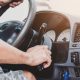 Mão de motorista girando a chave na ignição de um carro, com o volante e o painel de instrumentos ao fundo.