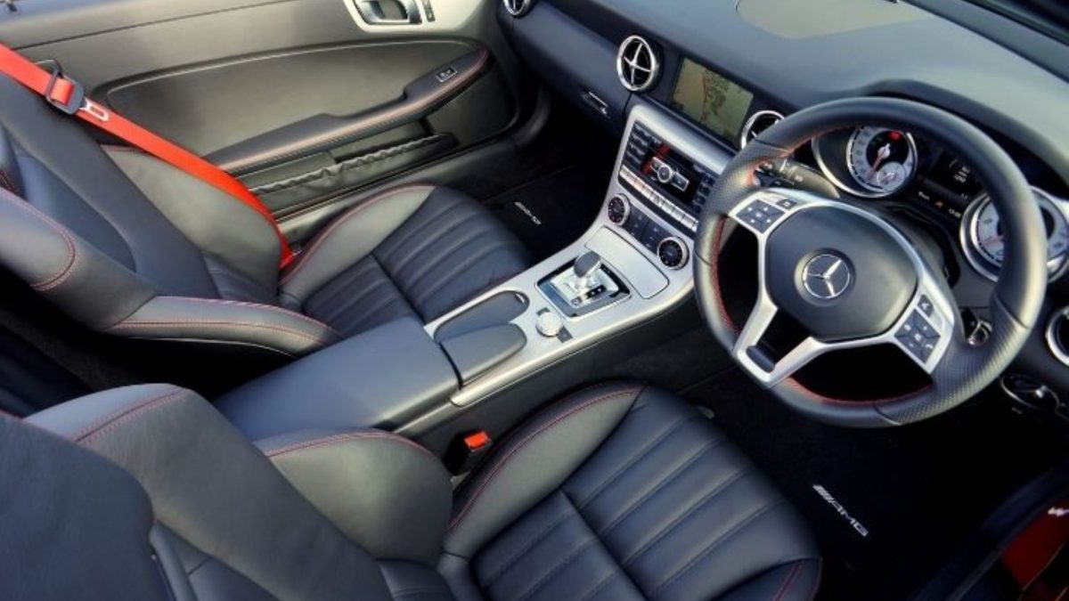 Interior de carro esportivo com bancos de couro preto, costura vermelha contrastante, cinto de segurança vermelho e volante multifuncional com câmbio automático ao centro.
