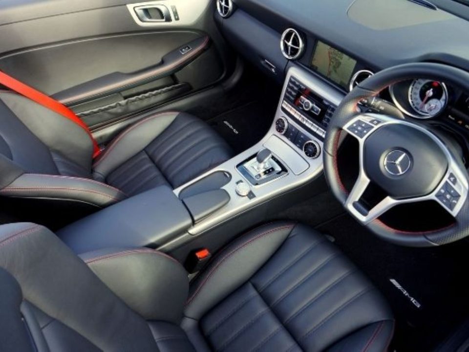 Interior de carro esportivo com bancos de couro preto, costura vermelha contrastante, cinto de segurança vermelho e volante multifuncional com câmbio automático ao centro.