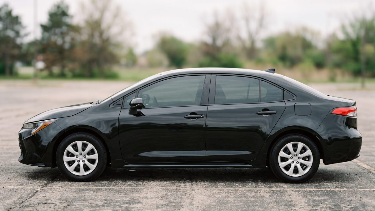 Toyota Corolla preto conservado e limpo, em vista lateral, estacionado em área aberta.