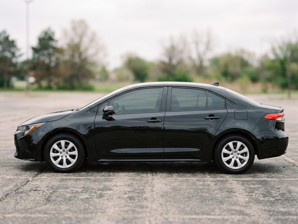 Toyota Corolla preto conservado e limpo, em vista lateral, estacionado em área aberta.