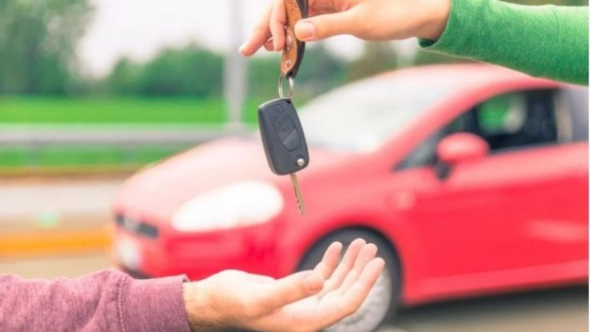 Mão entregando chave de carro para outra pessoa, com carro vermelho desfocado ao fundo, representando a venda de um veículo.
