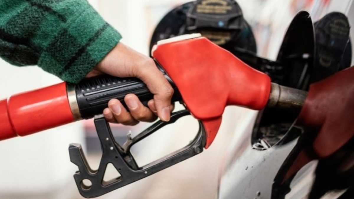 Mão segurando o bico vermelho da bomba de combustível durante o abastecimento de um carro branco.