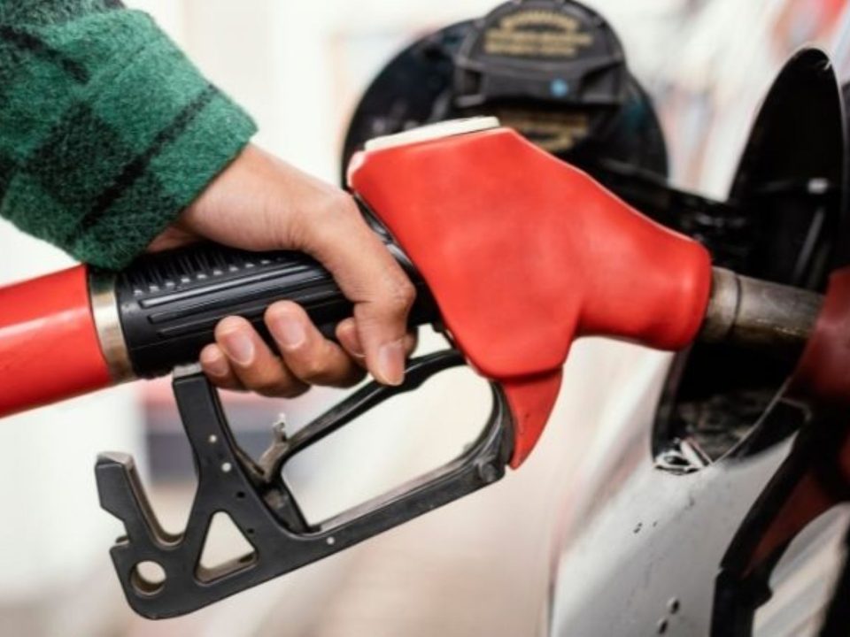 Mão segurando o bico vermelho da bomba de combustível durante o abastecimento de um carro branco.