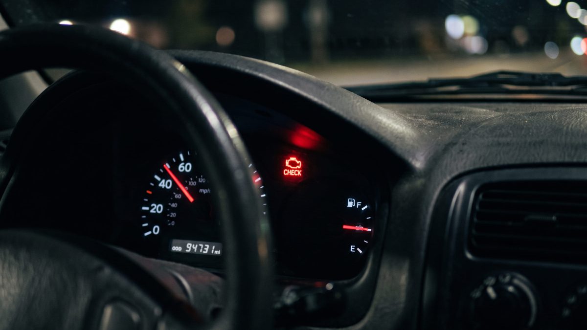 Painel de carro à noite com o ícone de alerta do motor aceso em vermelho, ao lado do velocímetro e do indicador de combustível.