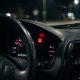 Painel de carro à noite com o ícone de alerta do motor aceso em vermelho, ao lado do velocímetro e do indicador de combustível.