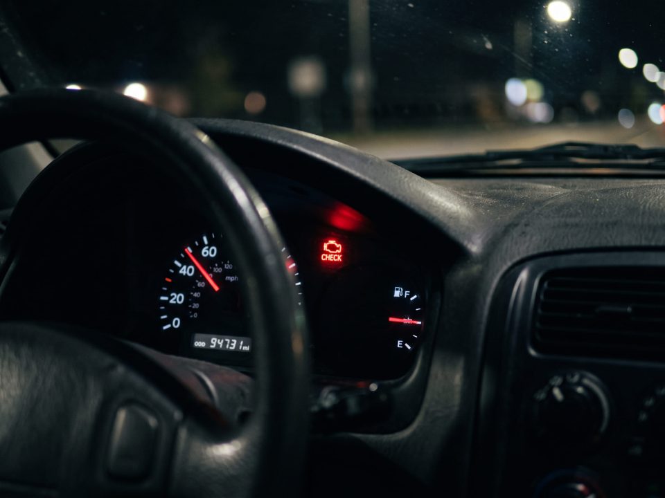 Painel de carro à noite com o ícone de alerta do motor aceso em vermelho, ao lado do velocímetro e do indicador de combustível.