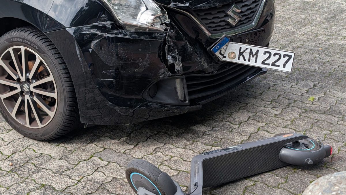 Carro preto com para-choque dianteiro danificado após colisão com patinete elétrico.