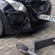 Carro preto com para-choque dianteiro danificado após colisão com patinete elétrico.