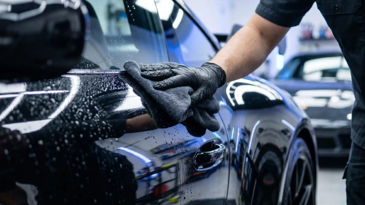 Profissional de estética automotiva com luvas pretas polindo a porta do motorista de um carro com pano de microfibra
