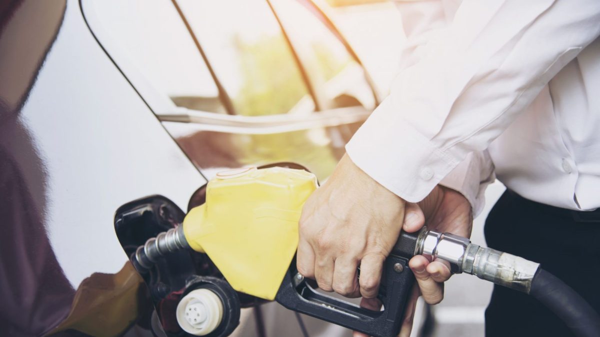 Homem abastecendo o carro com o bico da bomba de combustível em um posto de gasolina.