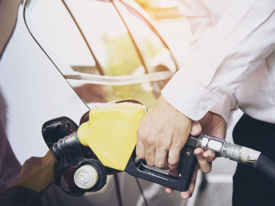 Homem abastecendo o carro com o bico da bomba de combustível em um posto de gasolina.