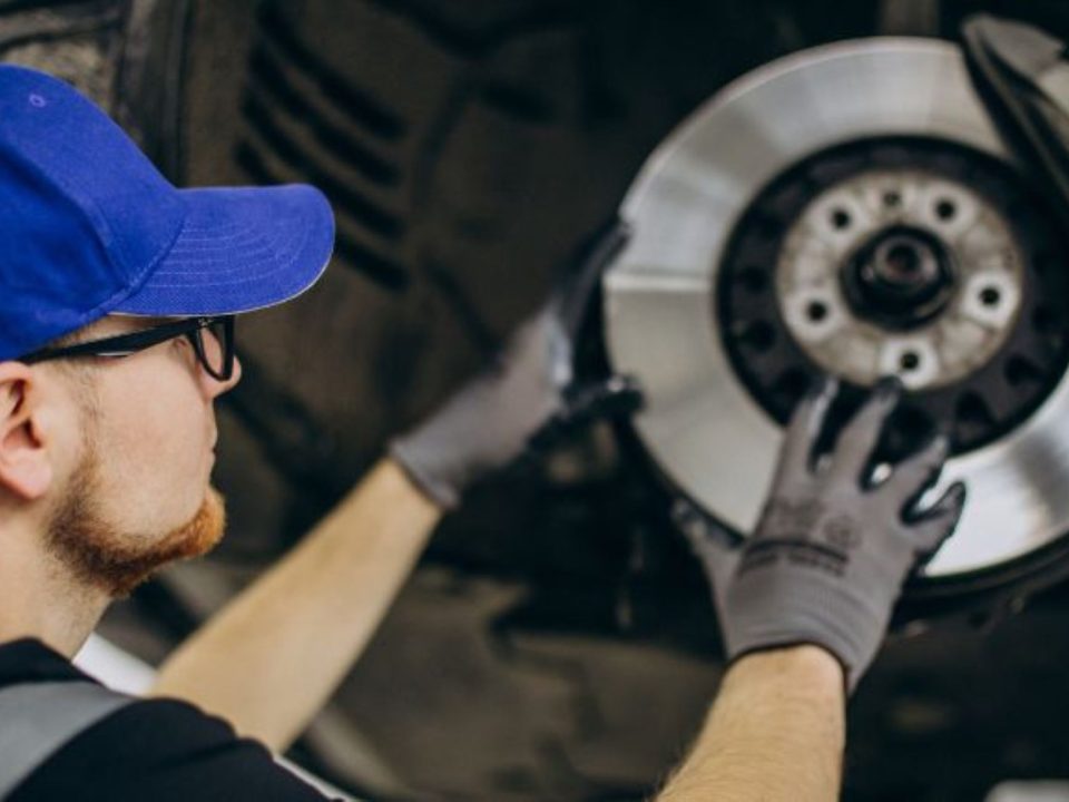 Mecânico com boné azul e luvas de proteção segurando e instalando um disco de freio em um carro.
