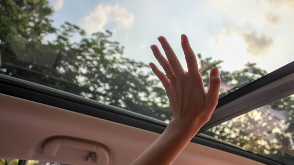 Mão próxima ao teto solar panorâmico de um carro, com luz natural entrando pela cabine.