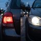 Imagem dividida mostrando a lanterna traseira vermelha acesa à esquerda e o farol dianteiro branco aceso à direita de um carro, ao entardecer.