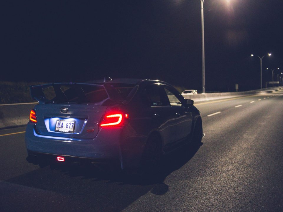 Vista traseira de carro escuro com lanterna de placa iluminada e luz de freio vermelha acesa.