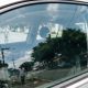 Vidro lateral dianteiro de carro fechado com reflexo de rua urbana e marcas de uso na superfície do vidro.