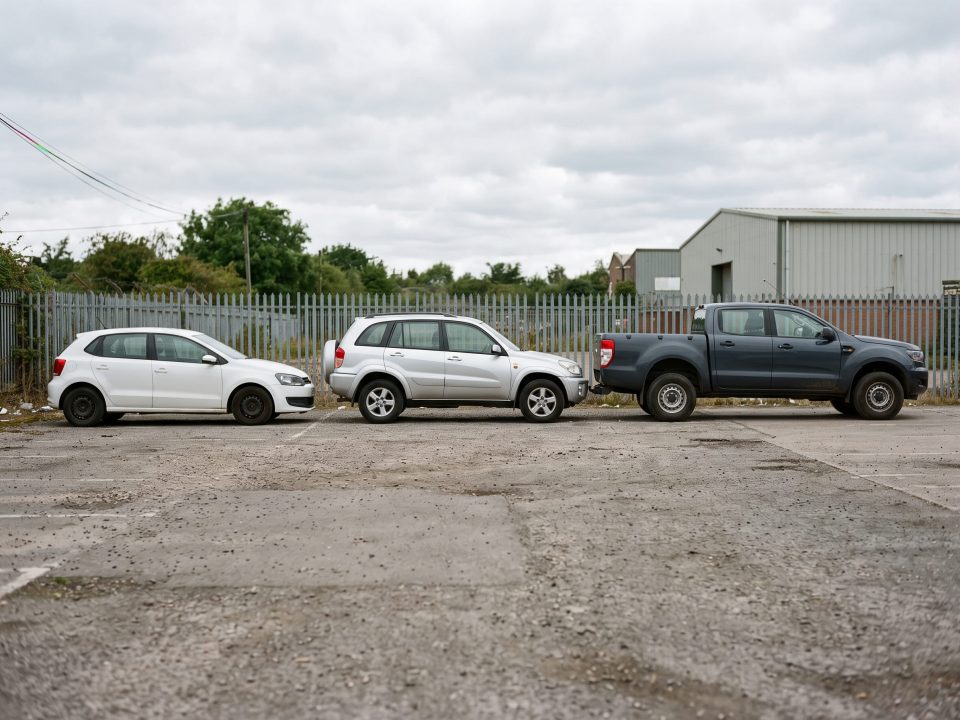 Três carros lado a lado mostrando diferentes tipos de carroceria: hatch branco, SUV prata e picape cinza-escura.