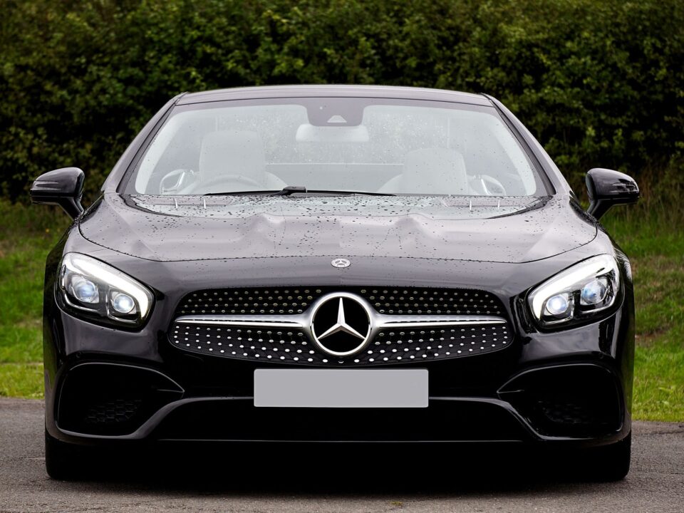 Vista frontal de um carro Mercedes-Benz preto estacionado ao ar livre, com gotas de água no para-brisa e na carroceria.