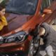 Homem de luvas calibrando o pneu dianteiro de um SUV laranja enquanto uma mulher observa apoiada no capô.