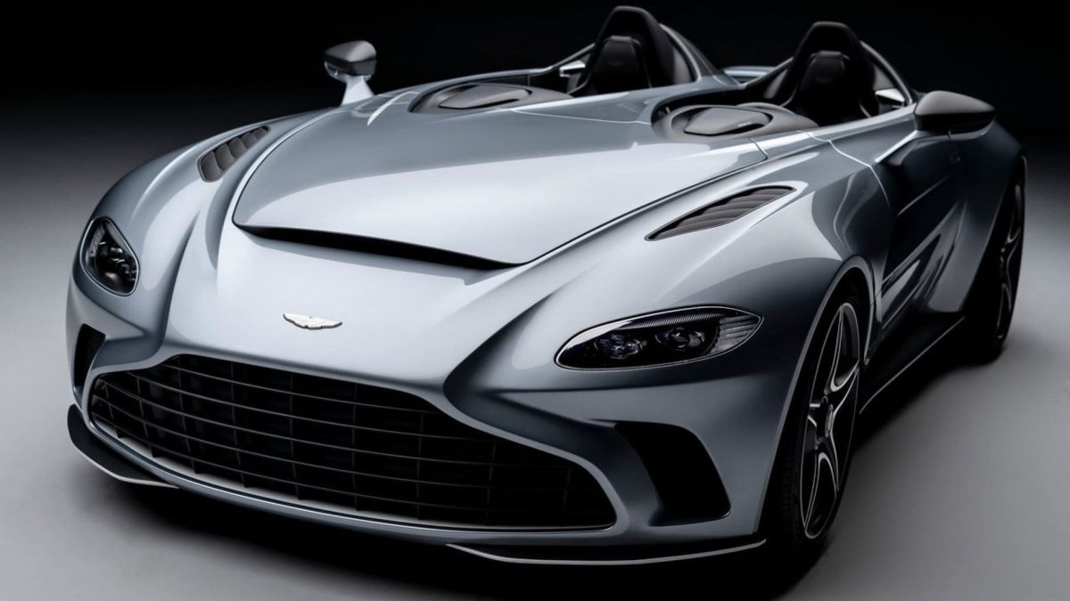 Foto em estúdio de um carro esportivo conversível cinza, com faróis dianteiros detalhados, grade frontal, design aerodinâmico moderno, sem a presença de para-brisa em fundo escuro e iluminação suave.