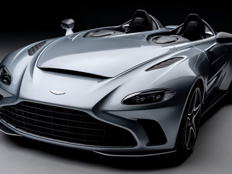 Foto em estúdio de um carro esportivo conversível cinza, com faróis dianteiros detalhados, grade frontal, design aerodinâmico moderno, sem a presença de para-brisa em fundo escuro e iluminação suave.