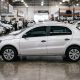 Carro hatch cinza fotografado de perfil dentro de uma loja de veículos seminovos, com outros carros desfocados ao fundo