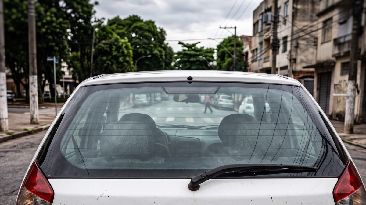 Vista traseira de um carro branco com o vidro vigia íntegro estacionado na rua.