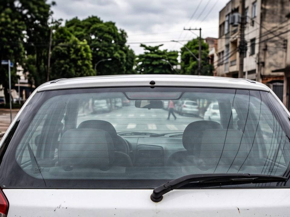 Vista traseira de um carro branco com o vidro vigia íntegro estacionado na rua.