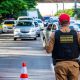 Policial militar rodoviário realiza fiscalização de veículos em uma via com cones de sinalização.