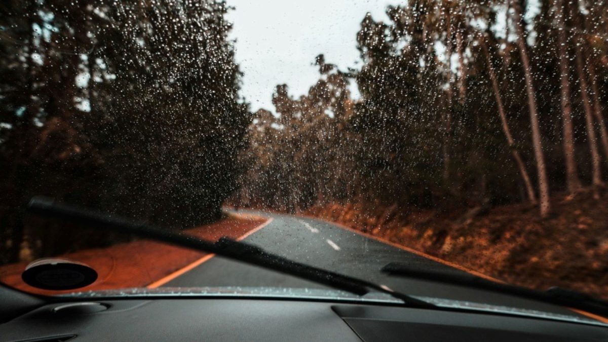 Para-brisa molhado pela chuva com palhetas do limpador em funcionamento durante trajeto em estrada.