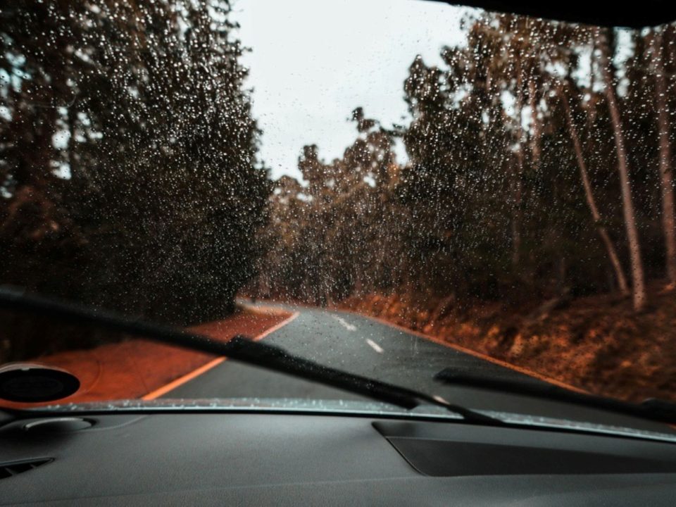 Para-brisa molhado pela chuva com palhetas do limpador em funcionamento durante trajeto em estrada.