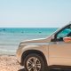 SUV prata estacionado na areia da praia, perto do mar, exposto à maresia.