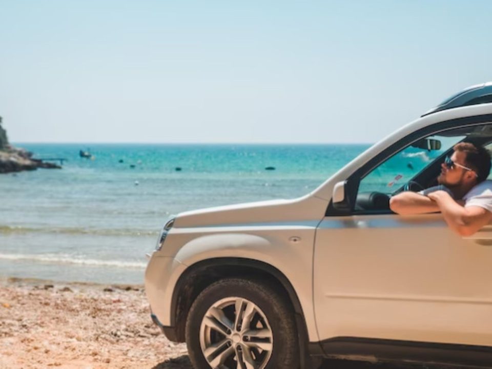 SUV prata estacionado na areia da praia, perto do mar, exposto à maresia.