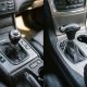 Comparação lado a lado entre alavanca de câmbio manual à esquerda e alavanca de câmbio automático à direita, ambas dentro do console central do carro.