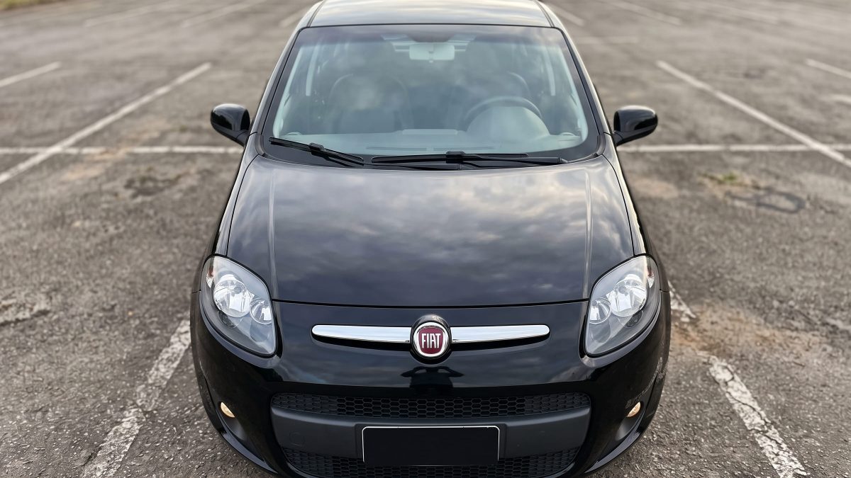 Vista frontal e elevada do capô de um Fiat Palio preto, com a grade cromada e os faróis na parte de baixo.
