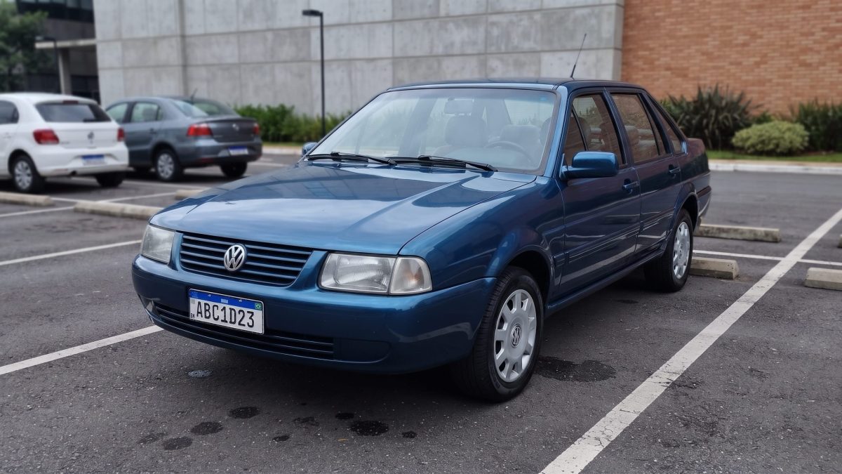 Volkswagen Santana azul estacionado em vaga de estacionamento, com outros carros ao fundo.
