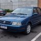 Volkswagen Santana azul estacionado em vaga de estacionamento, com outros carros ao fundo.
