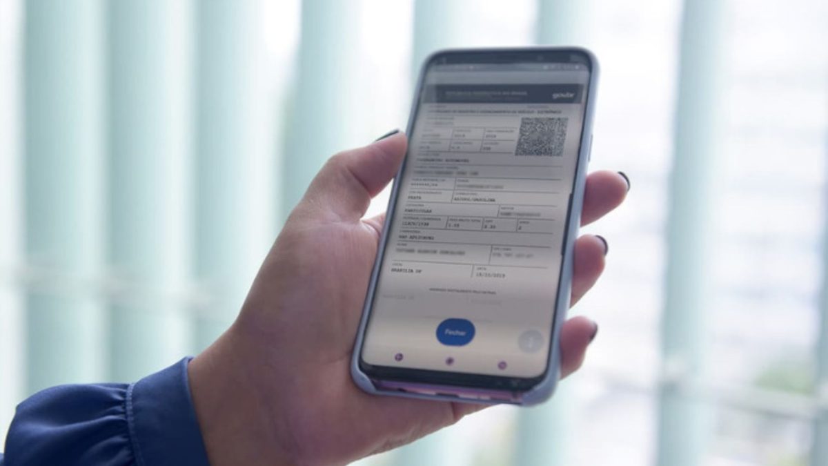 Mão segurando um smartphone com a tela do CRLV Digital aberta, exibindo o QR Code de autenticação do documento.