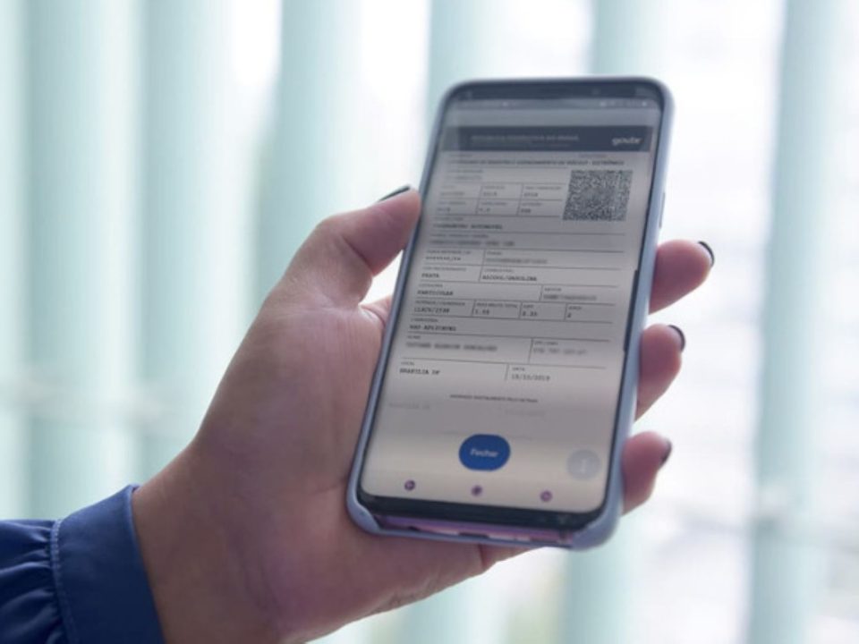 Mão segurando um smartphone com a tela do CRLV Digital aberta, exibindo o QR Code de autenticação do documento.