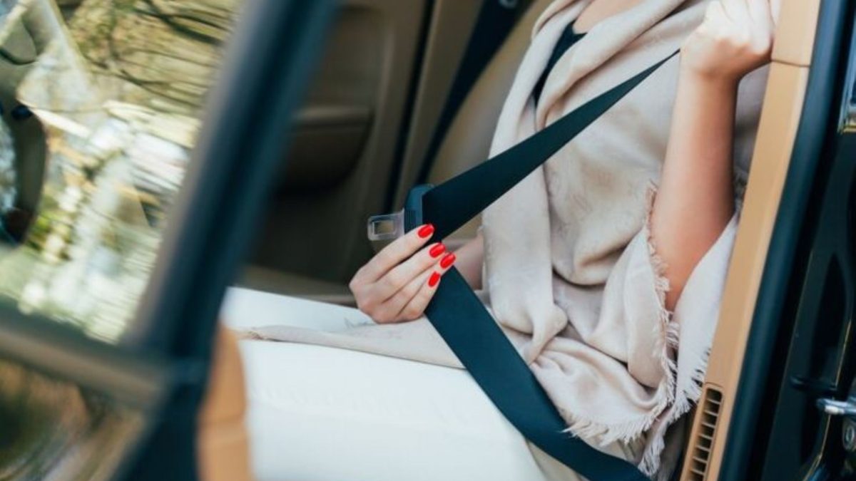 Mulher afivelando o cinto de segurança no banco traseiro do carro.