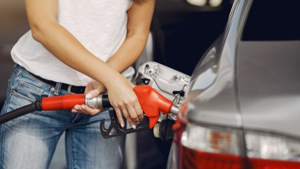 Mulher abastecendo um carro prata com bico de combustível vermelho no posto.