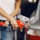 Mulher abastecendo um carro prata com bico de combustível vermelho no posto.