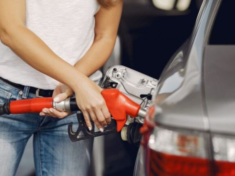 Mulher abastecendo um carro prata com bico de combustível vermelho no posto.